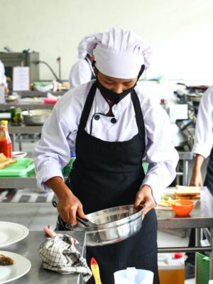 Chefs in masks preparing food in a commercial kitchen, emphasizing hygiene and teamwork.