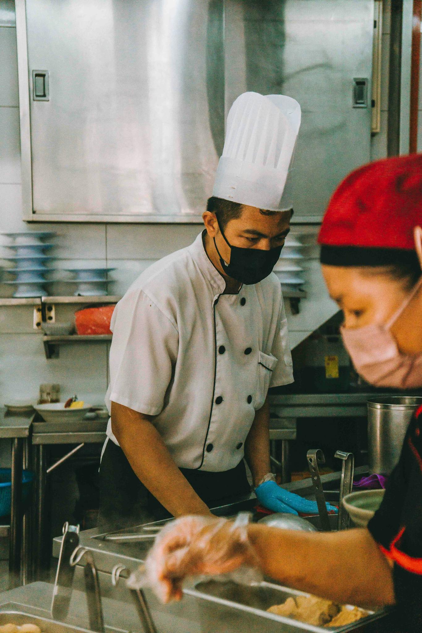 Chefs wearing masks prepare food in a busy Kuala Lumpur kitchen highlighting culinary arts.