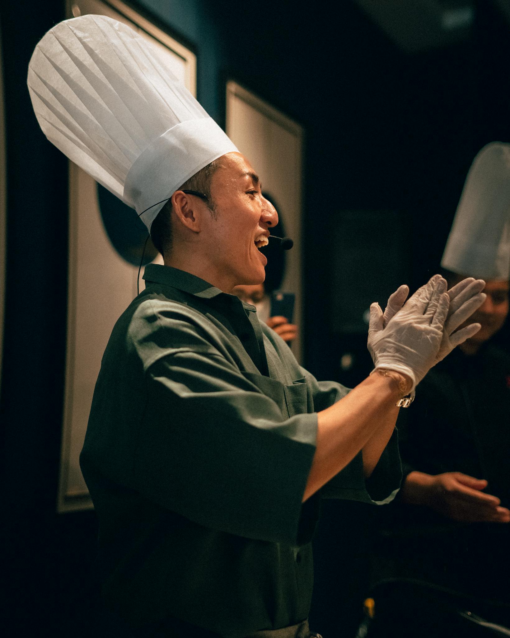 Smiling Asian chef claps in a commercial kitchen environment, showcasing culinary joy.
