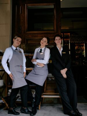 Three restaurant staff members in formal uniforms posing cheerfully in front of a restaurant.
